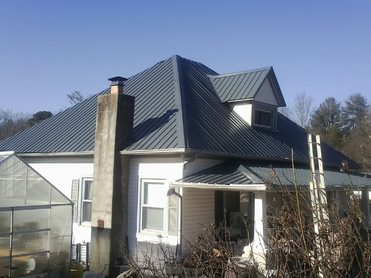 Dark blue standing seam metal roof on a white farmhouse with dormer — Slate & Tile Roof Repair by Roofing Brothers in Spofford