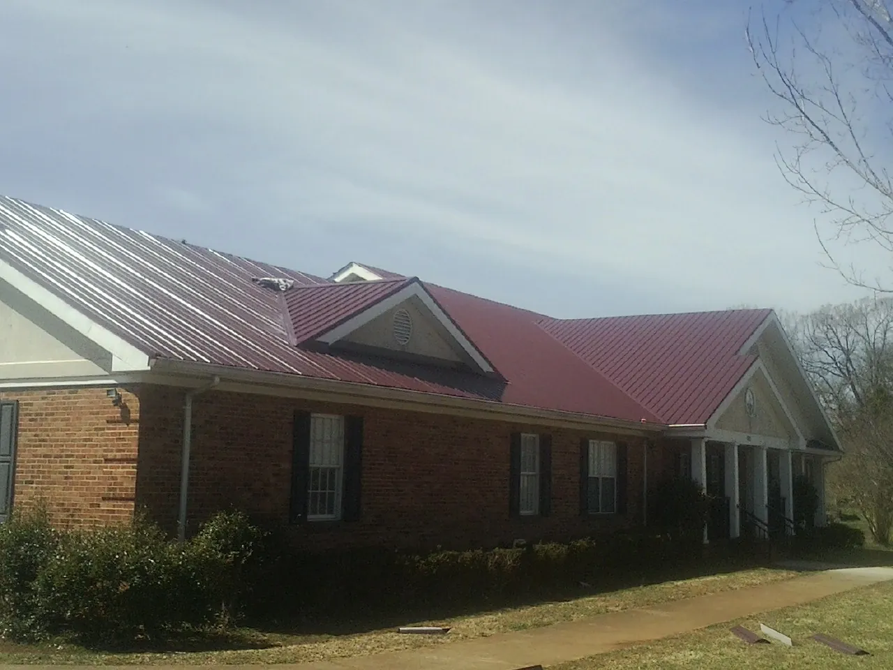 Red metal roof with gabled entries on a long brick building, from a Hail Damage Roof Repair job in Spofford
