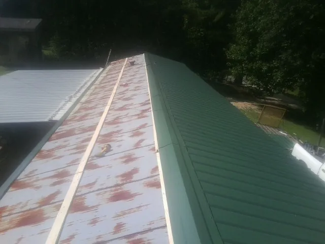 Old rusted panels beside newly installed green metal roofing — Wind Damage Roof Repair by Roofing Brothers in Spofford
