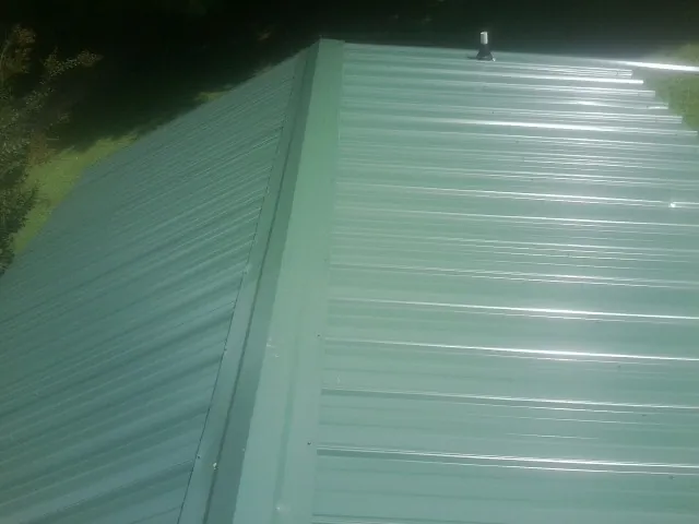 New green metal panels meeting at the ridge of a roof — Flat Roof Repair work by our crew in Spofford