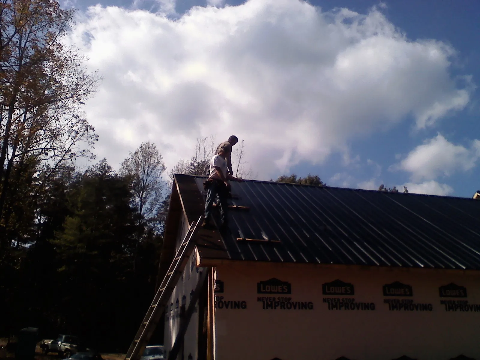 Roofer fastening dark metal panels high against a cloudy sky, from a Roof Inspection job in Spofford