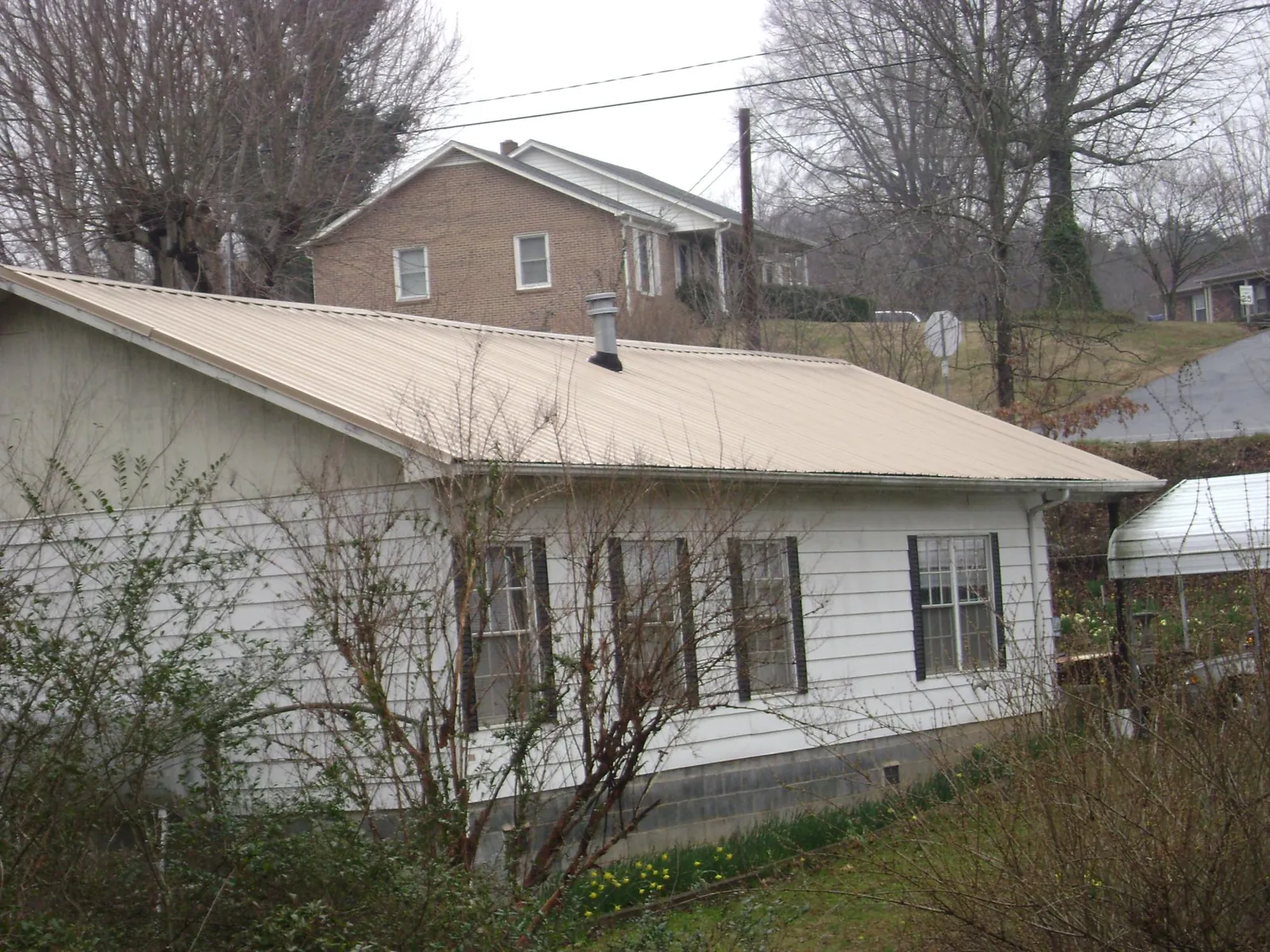 Tan metal roof on a white sided house set into a hillside — Commercial Roofing by Roofing Brothers in Spofford